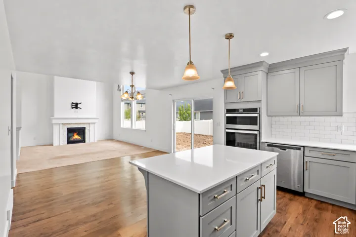 Kitchen featuring a central island with a quartz countertop, shaker-style cabinetry, stainless steel double wall ovens, and wood-finish flooring