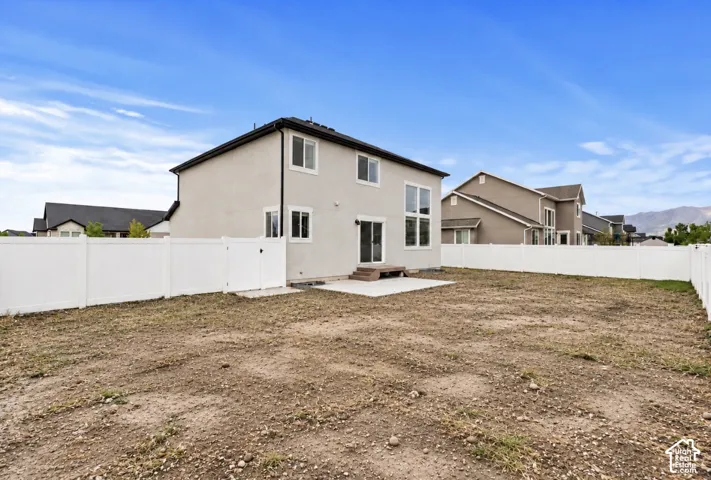 Two-story stucco exterior, concrete rear patio, white vinyl privacy fencing, and tall multi-pane windows
