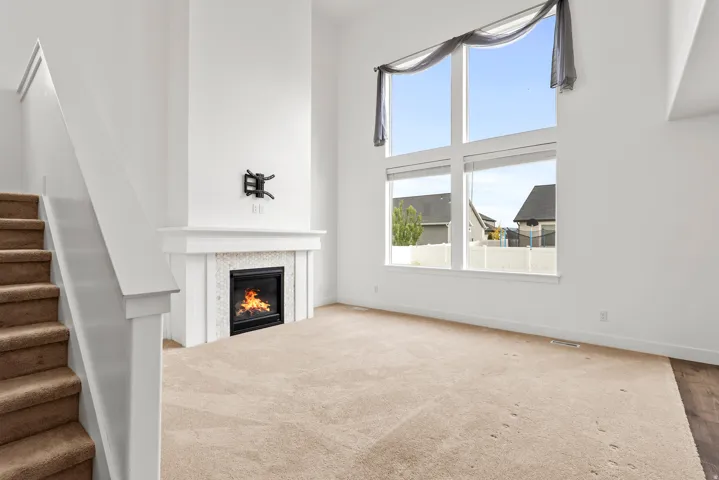 Two-story living room featuring a fireplace with a decorative tile surround and mantel, high ceilings, a prominent window arrangement, and carpeted flooring