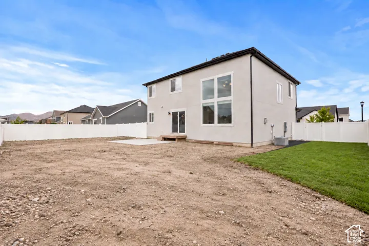 Two-story exterior featuring a light-toned stucco facade, expansive multi-pane windows, a sliding glass door, a paved patio, and perimeter white vinyl fencing