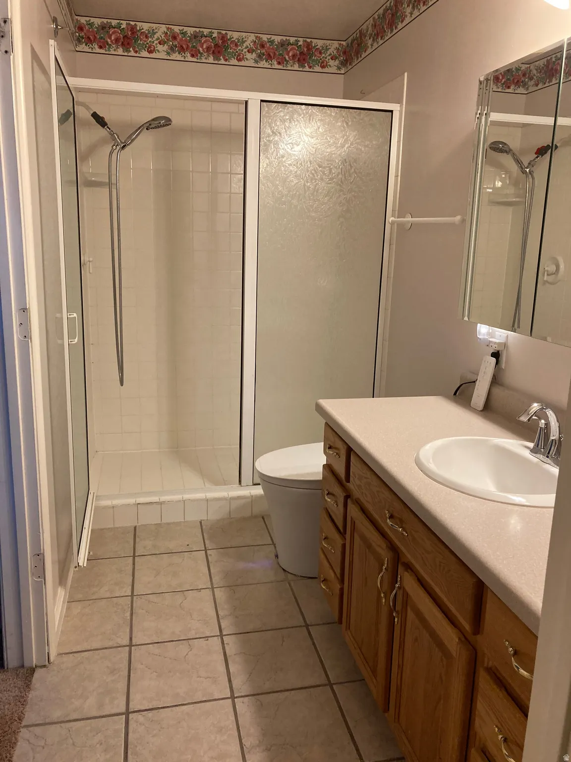 Bathroom featuring a glass-enclosed shower with white subway tile, a vanity with wood cabinetry and a light-toned countertop, a single basin sink with chrome fixtures, and neutral tile flooring