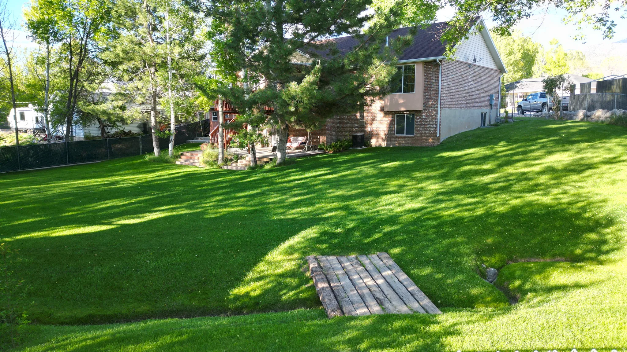 Expansive green lawn with mature trees and a charming wooden footbridge spanning a small stream