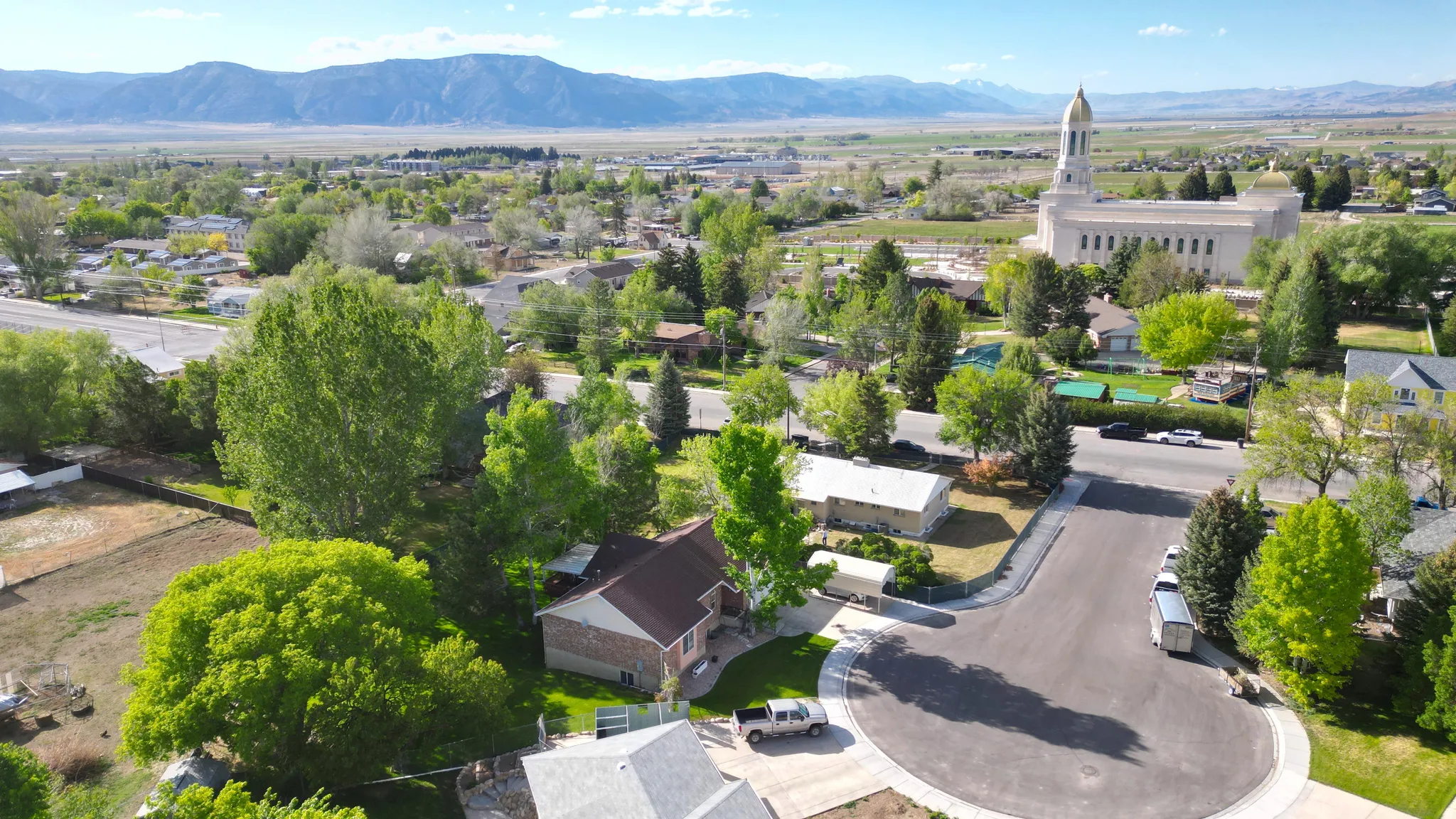 Aerial perspective showcasing a residential property with a brown roof and brick siding, bordered by mature trees and green landscaping