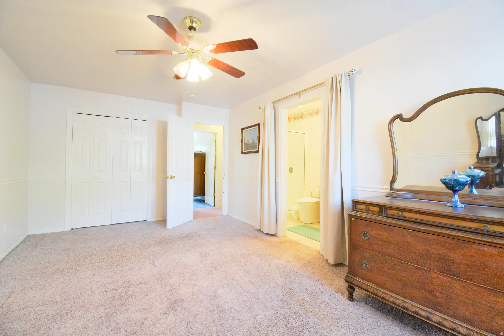 Carpeted room featuring a ceiling fan with light fixture, white bi-fold closet doors, and chair rail molding