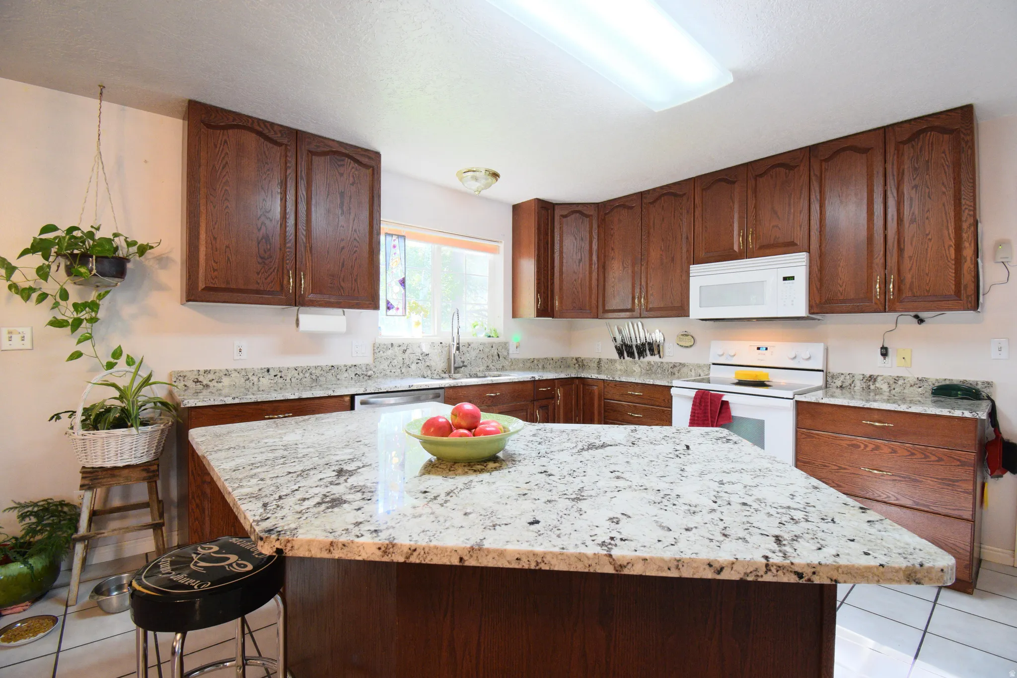 Kitchen featuring a large central island with a light-colored, patterned countertop, complementing perimeter countertops, wood cabinetry, a white electric range, and a built-in microwave