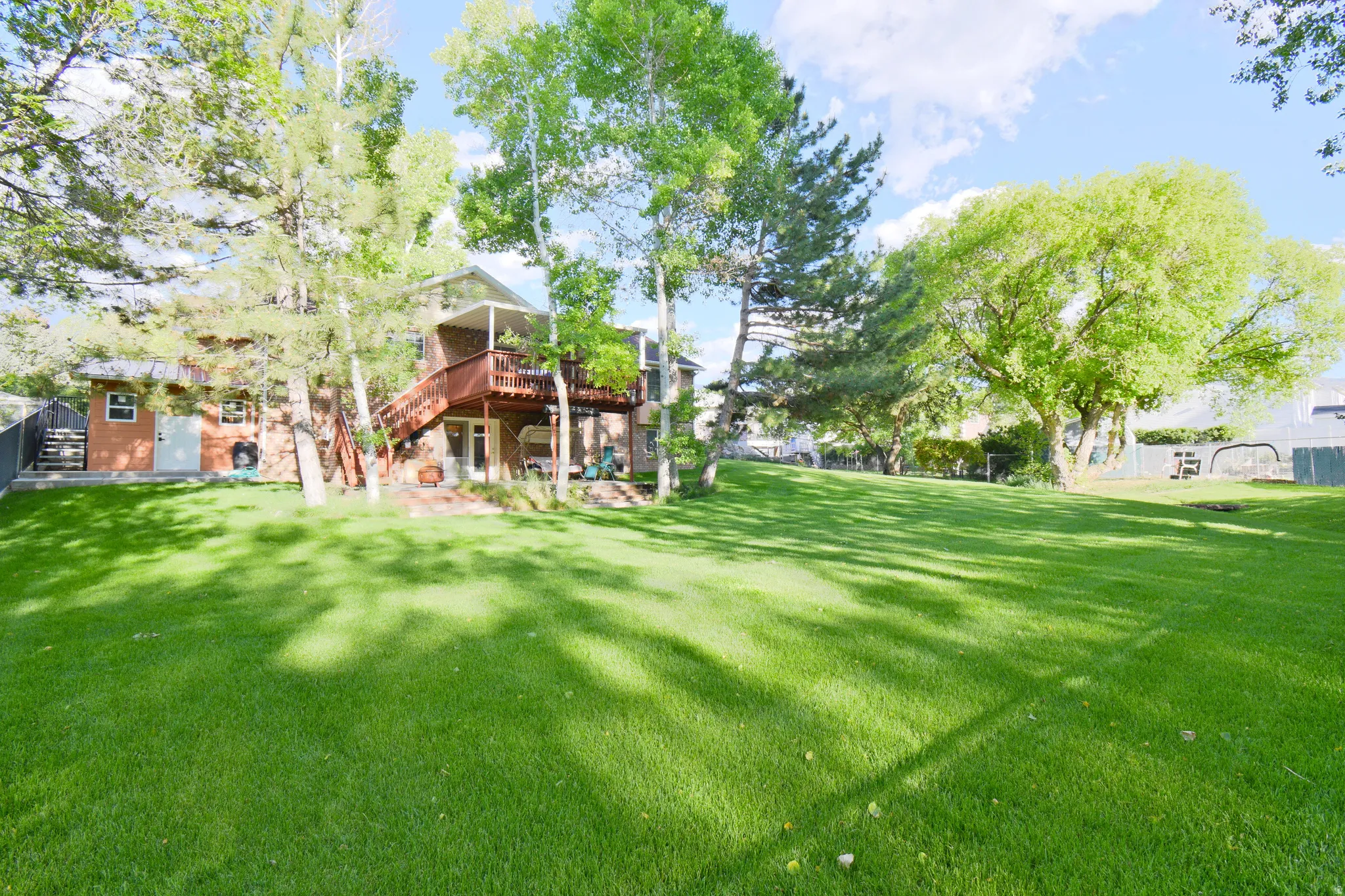 Spacious backyard featuring a manicured lawn, established shade trees, and a multi-level wood deck