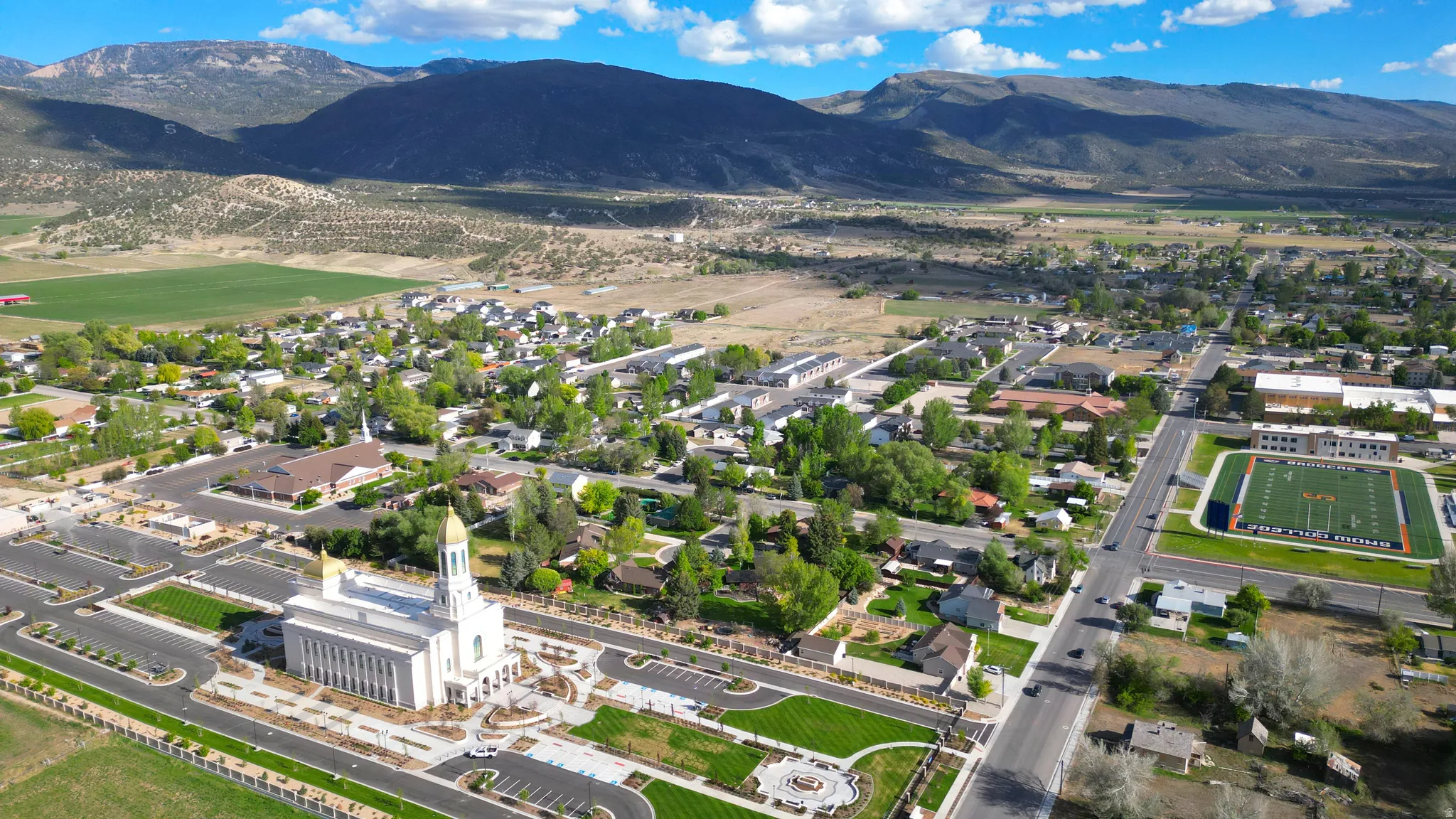 Aerial view of a community featuring a prominent central building with gold-colored spires, well-maintained landscaping, and surrounding residential areas