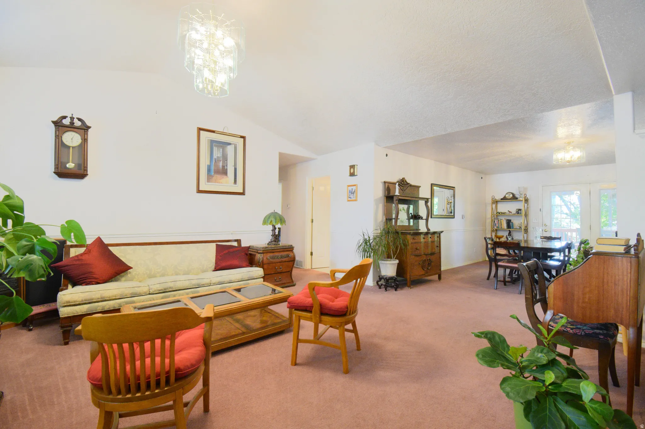 Vaulted ceilings accent a spacious living area featuring wall-to-wall carpeting and a decorative chandelier