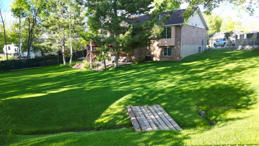 Expansive green lawn with mature trees and a charming wooden footbridge spanning a small stream