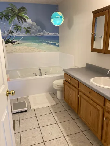 Bathroom featuring a built-in tub, a single vanity with a laminate countertop, oak-finish cabinetry, and square tile flooring