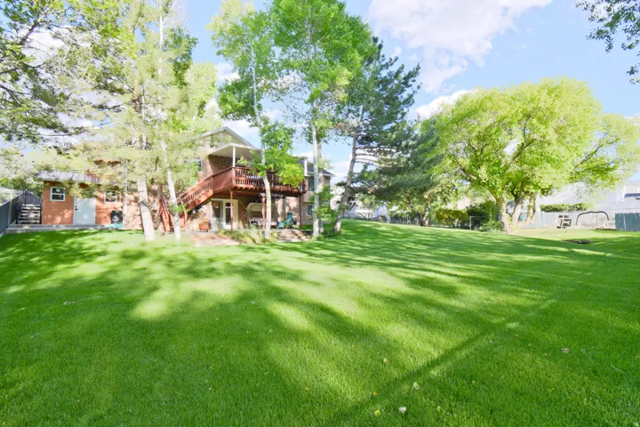 Spacious backyard featuring a manicured lawn, established shade trees, and a multi-level wood deck