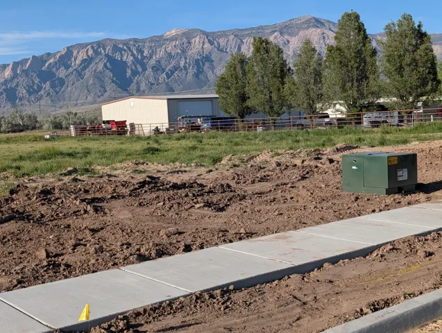Paved sidewalk bordering a cleared lot with distant mountain scenery