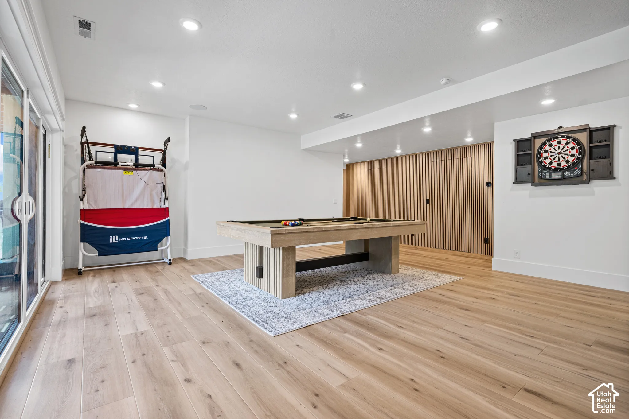 Spacious room featuring light wood-finish flooring, recessed lighting, and a modern dartboard cabinet