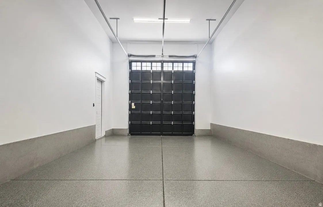 Spacious interior featuring a large black paneled door with window accents, light gray epoxy flooring, white walls, and a white side door
