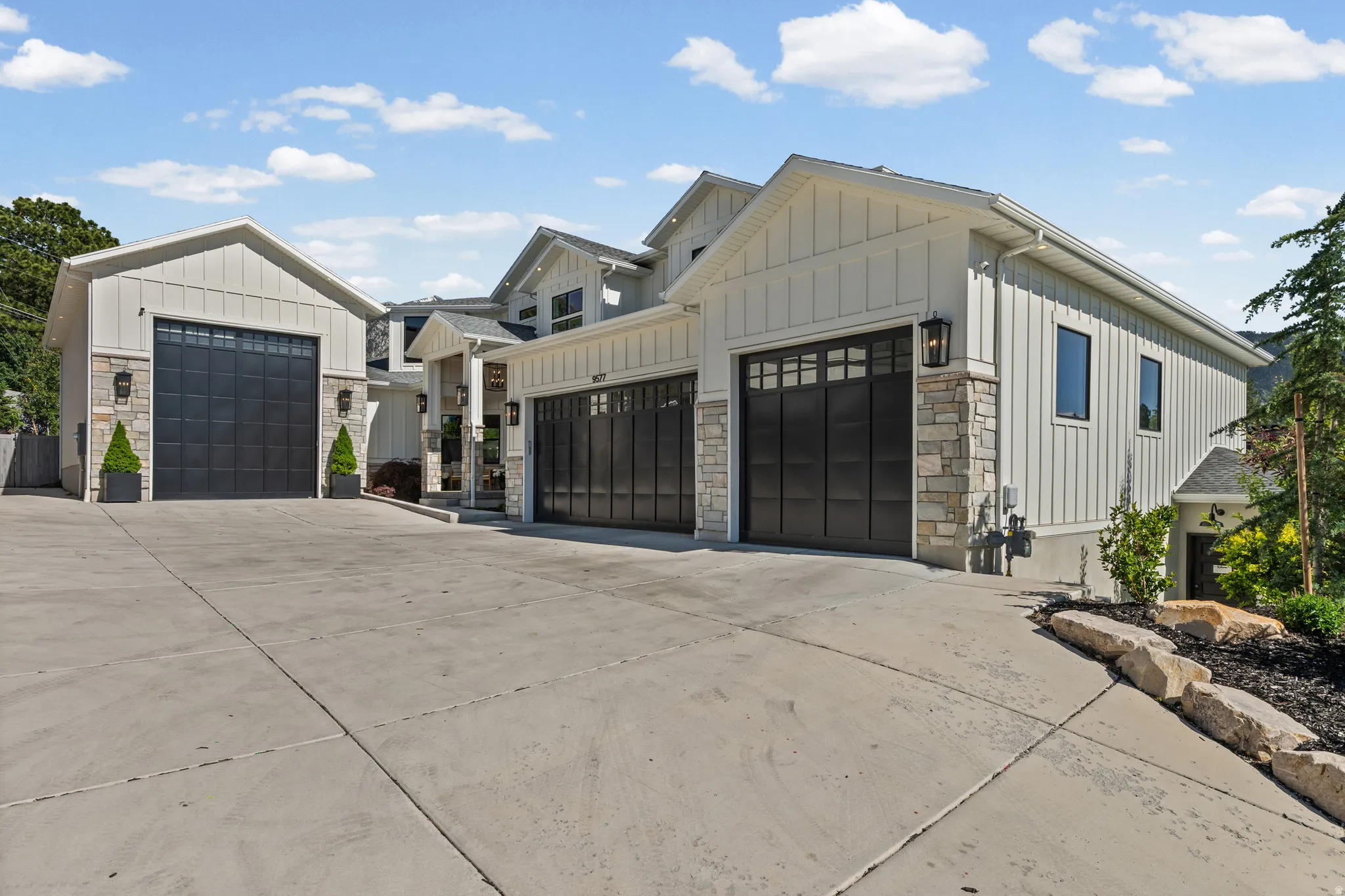 Modern farmhouse exterior featuring board and batten siding, stone accents, black-framed windows, multiple garage bays with dark paneled doors, and concrete driveway