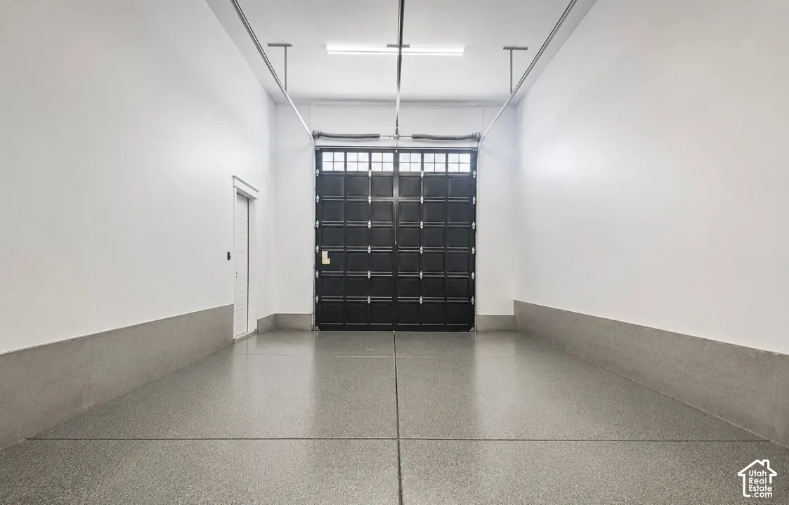Spacious interior featuring a large black paneled door with window accents, light gray epoxy flooring, white walls, and a white side door