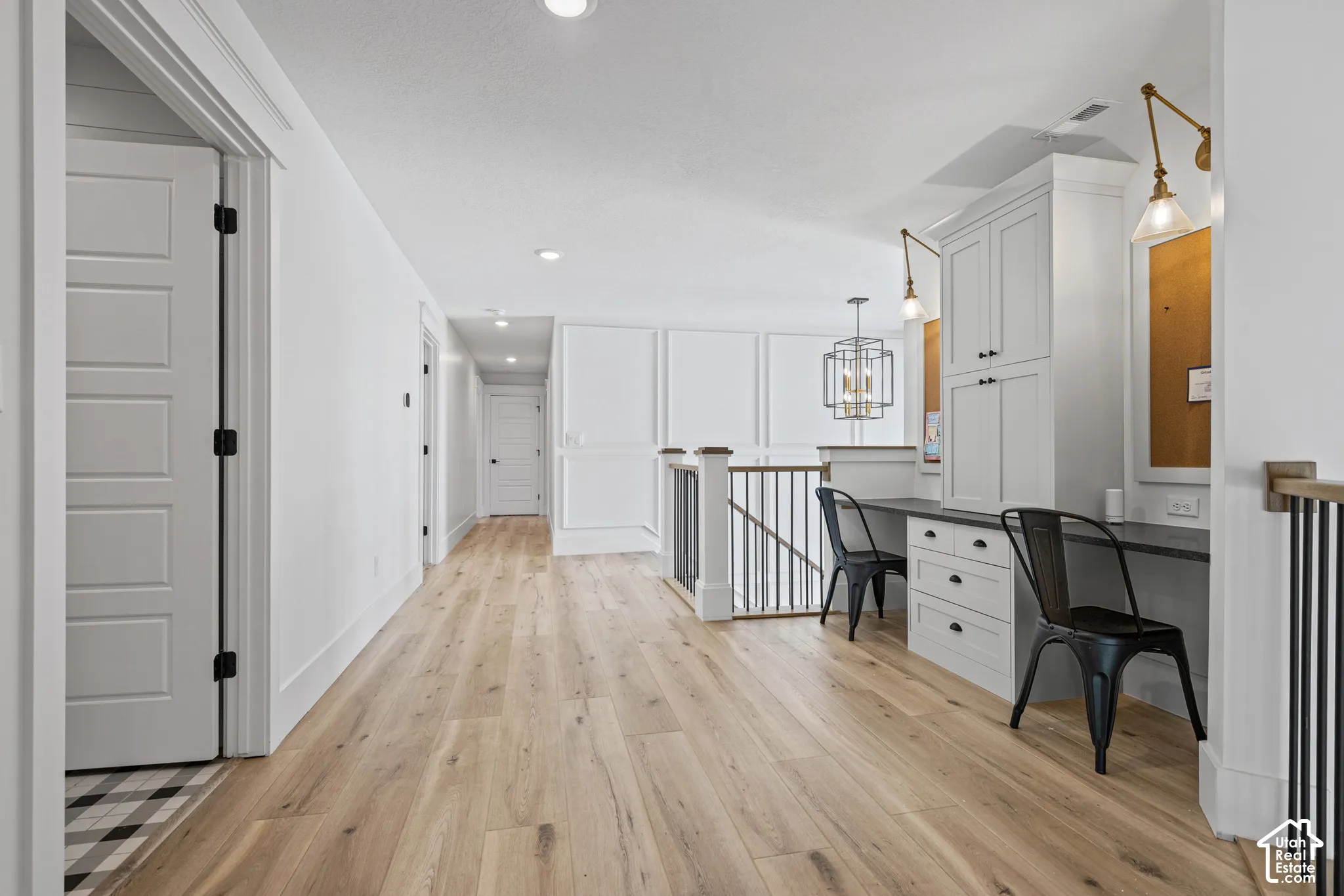 Hallway featuring wood-finish flooring, recessed lighting, and a built-in desk area with cabinetry, a dark countertop, and decorative wall sconces