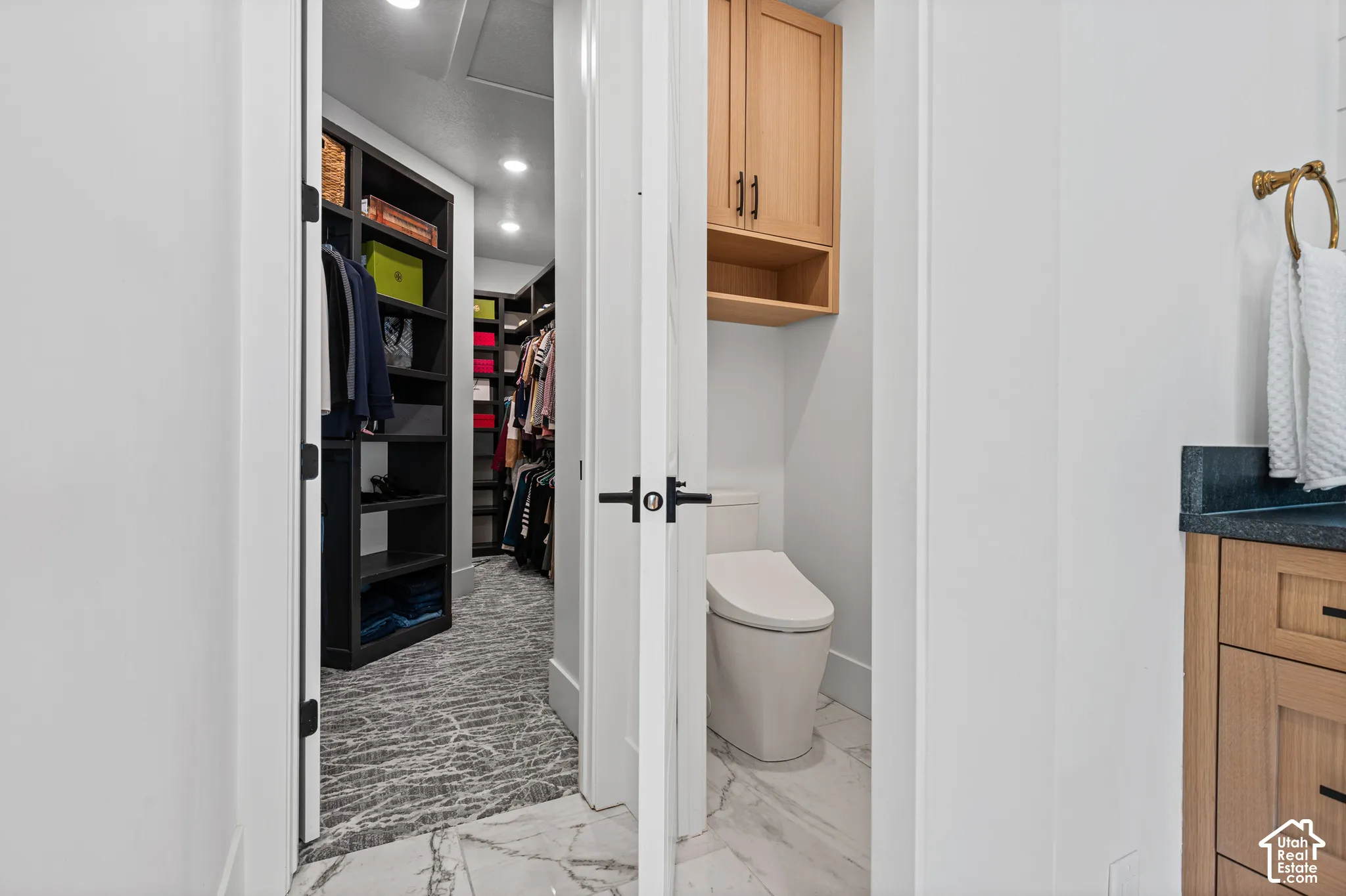 Walk-in closet with dark built-in shelving, patterned flooring, and recessed lighting, adjacent to a water closet featuring a toilet and overhead wood-finish cabinetry