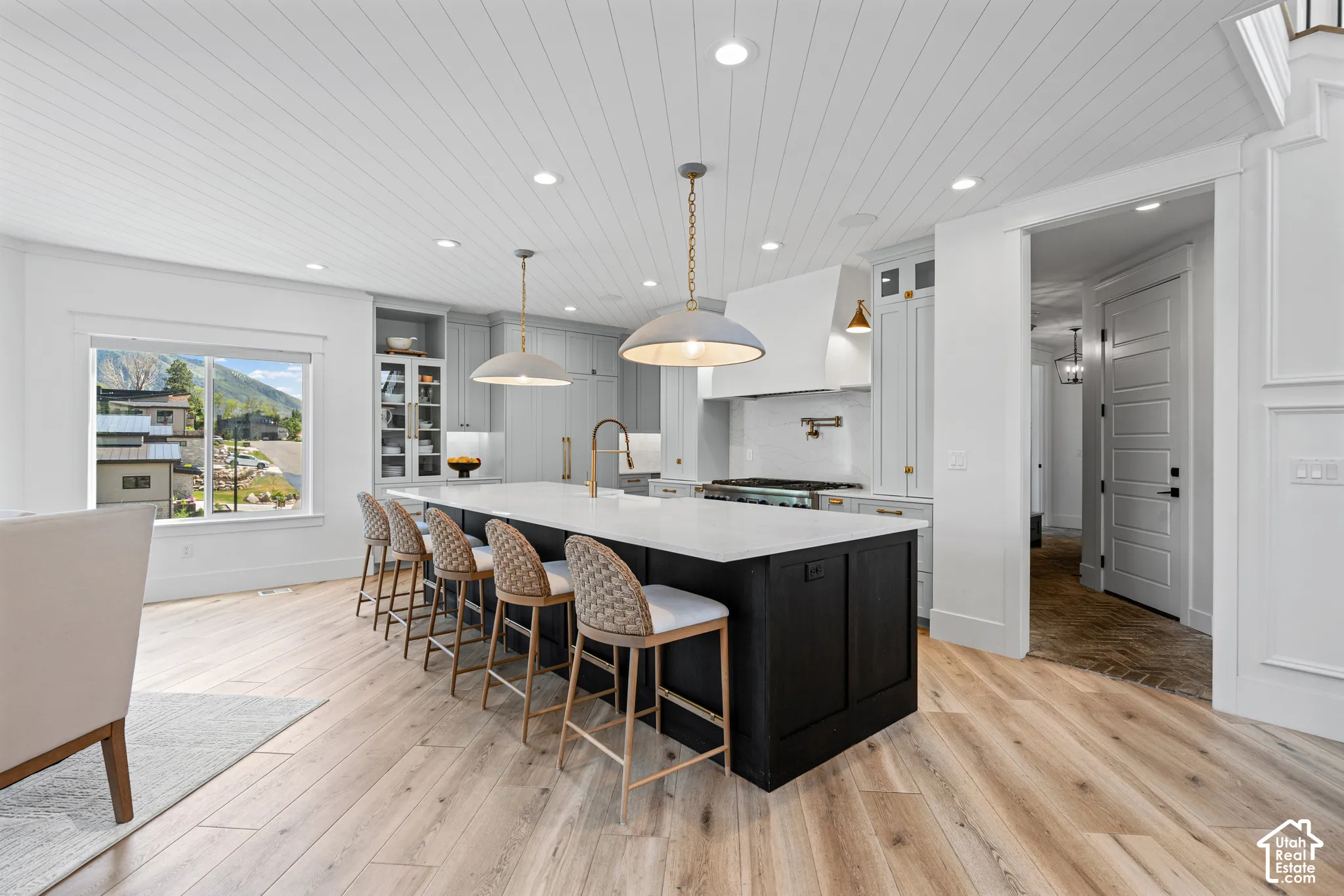 Spacious kitchen featuring a large island with seating, light wood-finish flooring, white shiplap ceiling, and light gray cabinetry