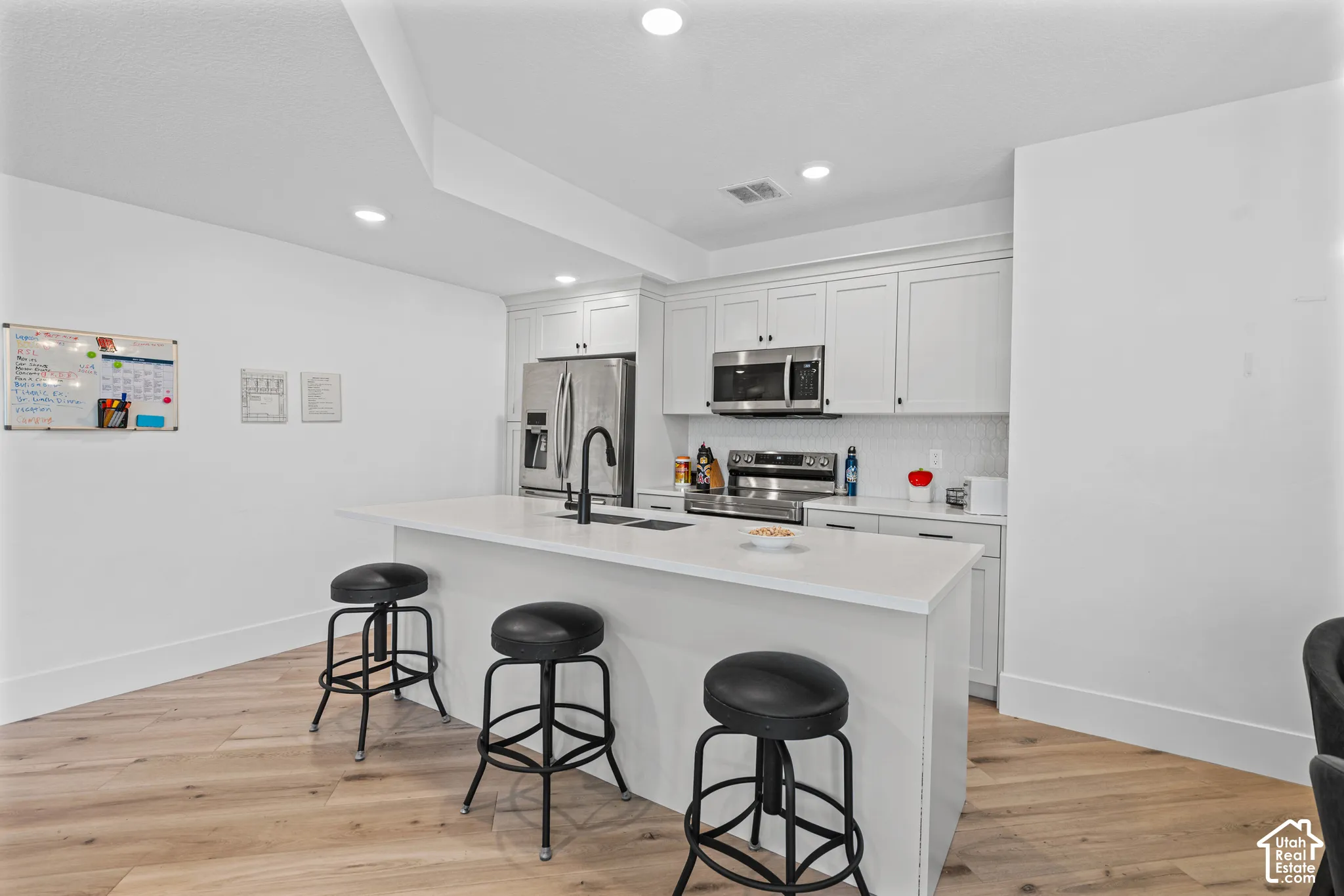 Bright kitchen featuring an expansive center island with seating, white shaker cabinetry, stainless steel appliances, and a tile backsplash