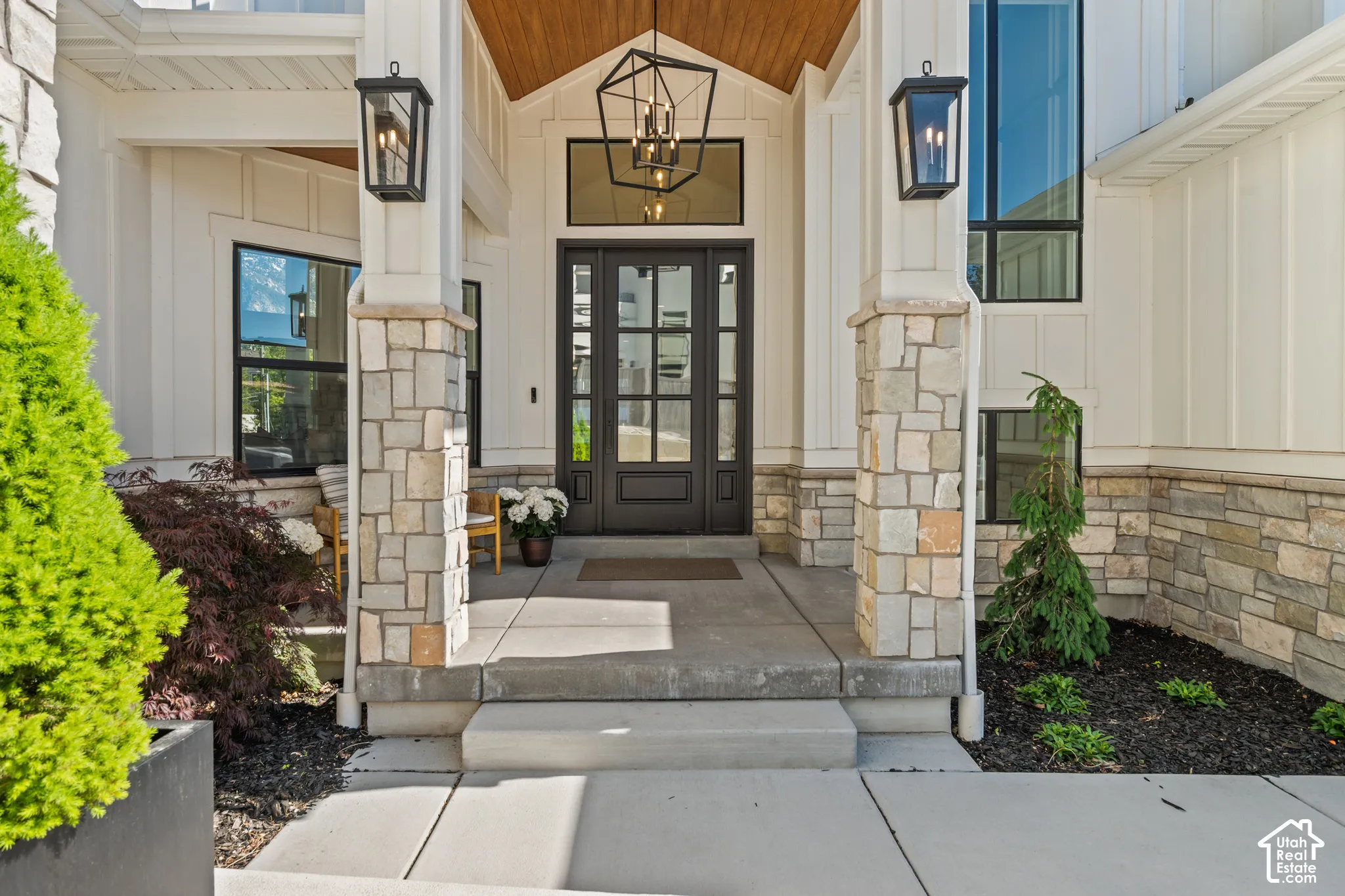 Entryway featuring a double door with glass panels, stone-clad pillars, board and batten siding, a wood-paneled ceiling, and large black-framed windows