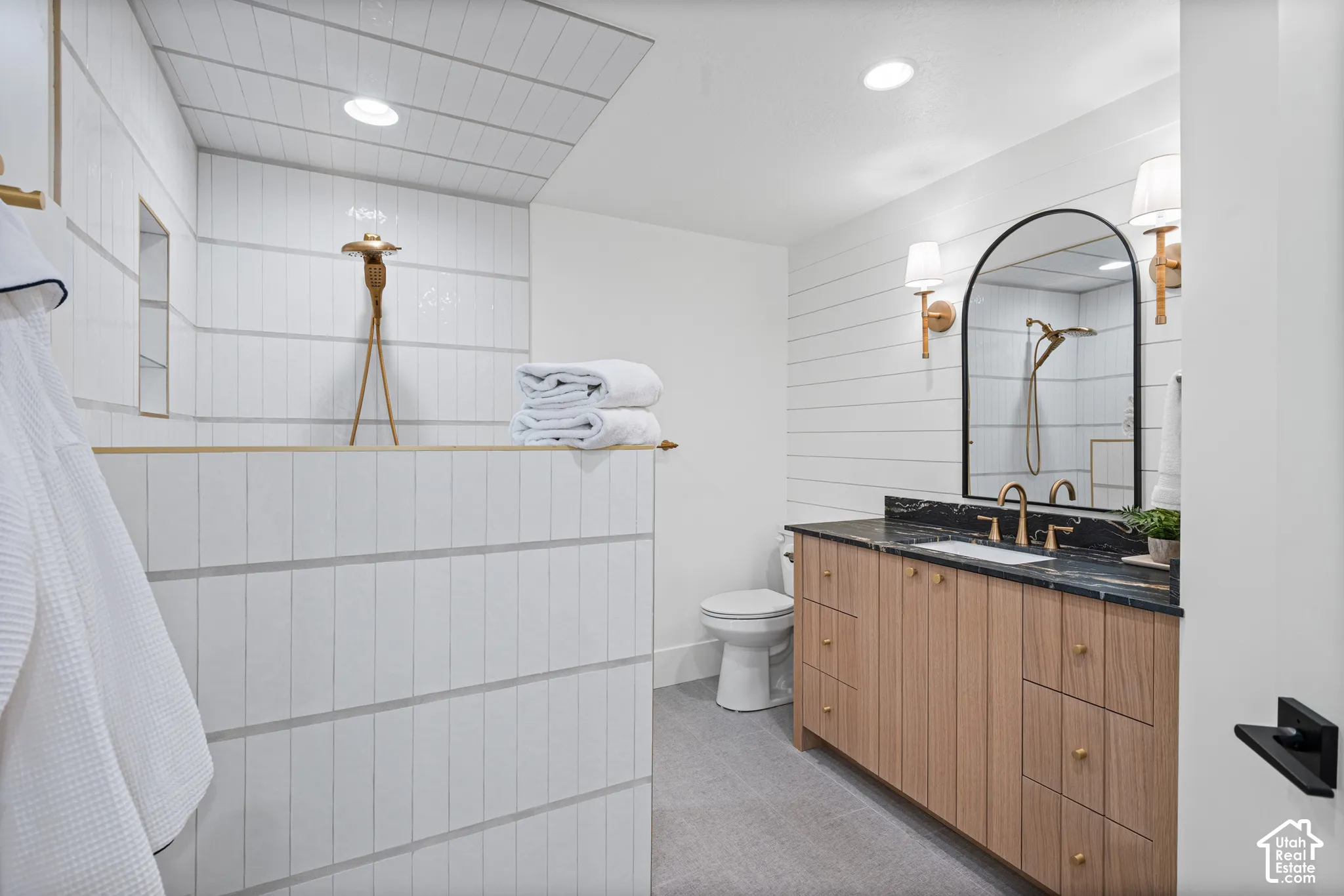 Contemporary bathroom featuring a light wood-finish vanity with a dark countertop and gold-tone hardware