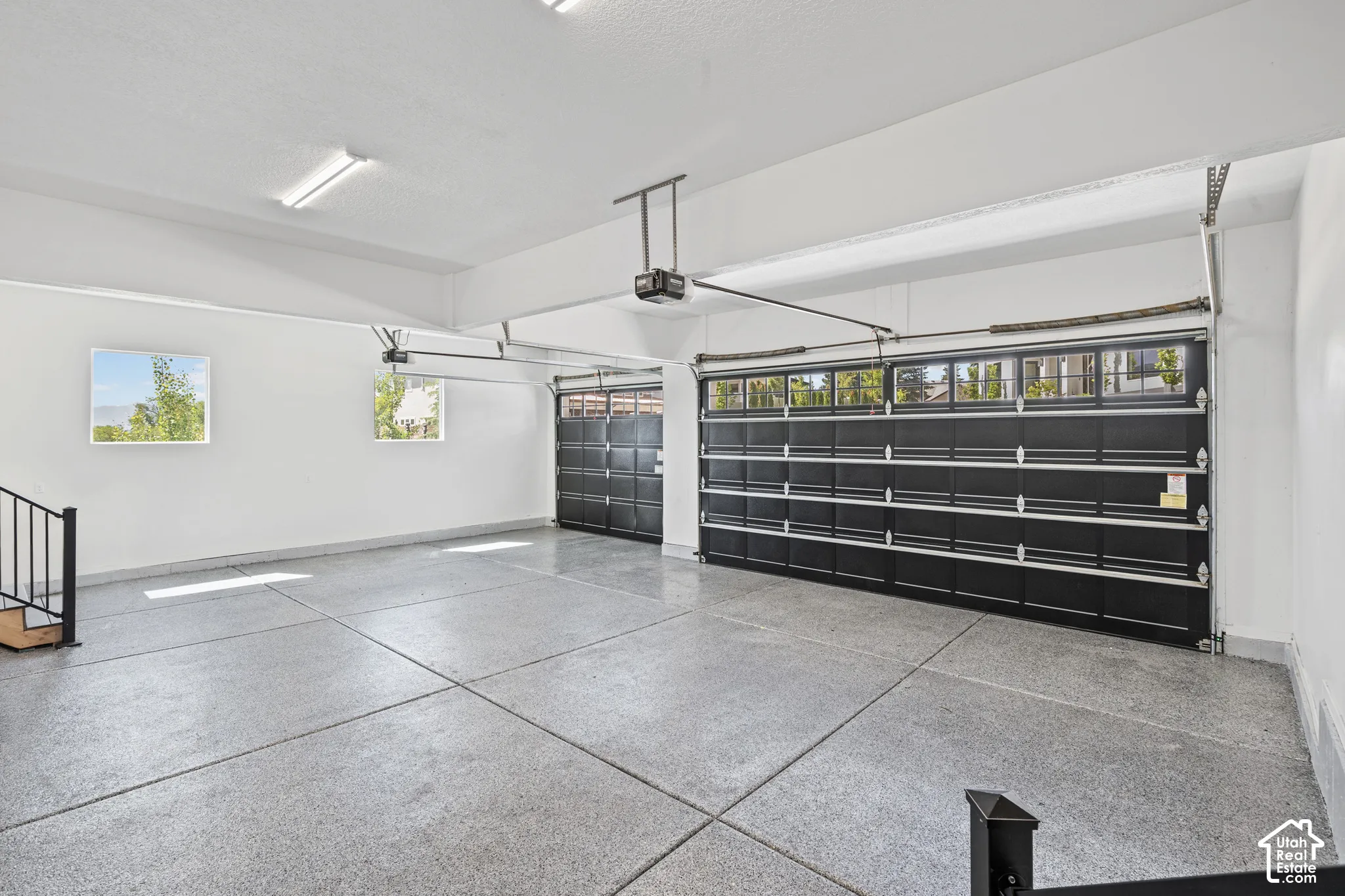 Spacious multi-car garage featuring epoxy-coated flooring, two overhead garage doors with frosted window panels, and multiple windows providing natural illumination