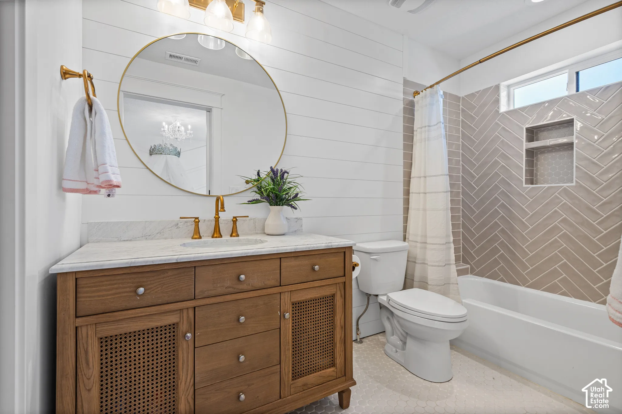 Bathroom featuring a wood-finish vanity with a light-colored countertop, gold-toned fixtures, a round framed mirror, and shiplap walls