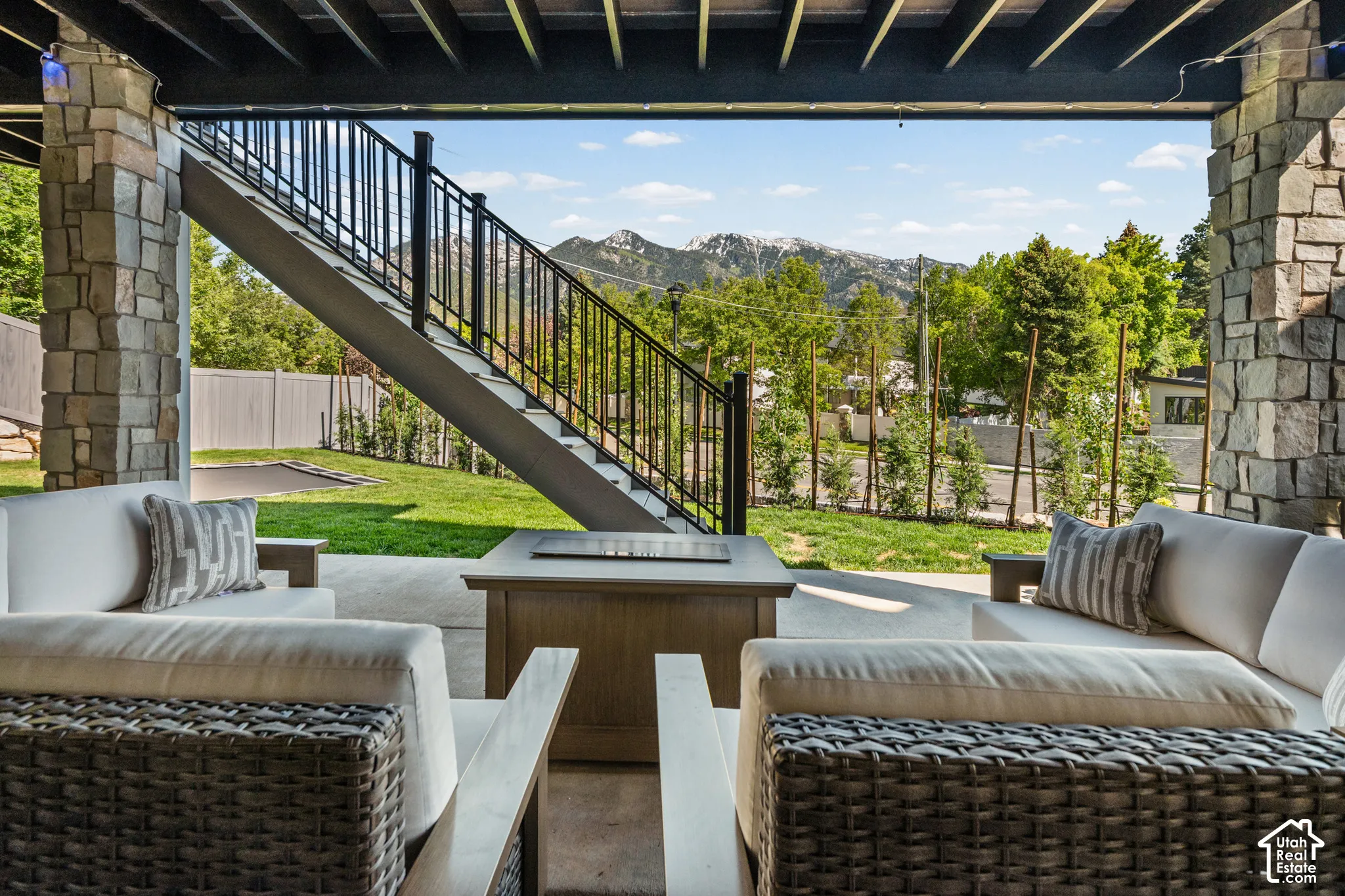 Covered patio featuring stone pillars, a concrete floor, an outdoor fire pit, and a prominent staircase with black metal railings leading to the upper level