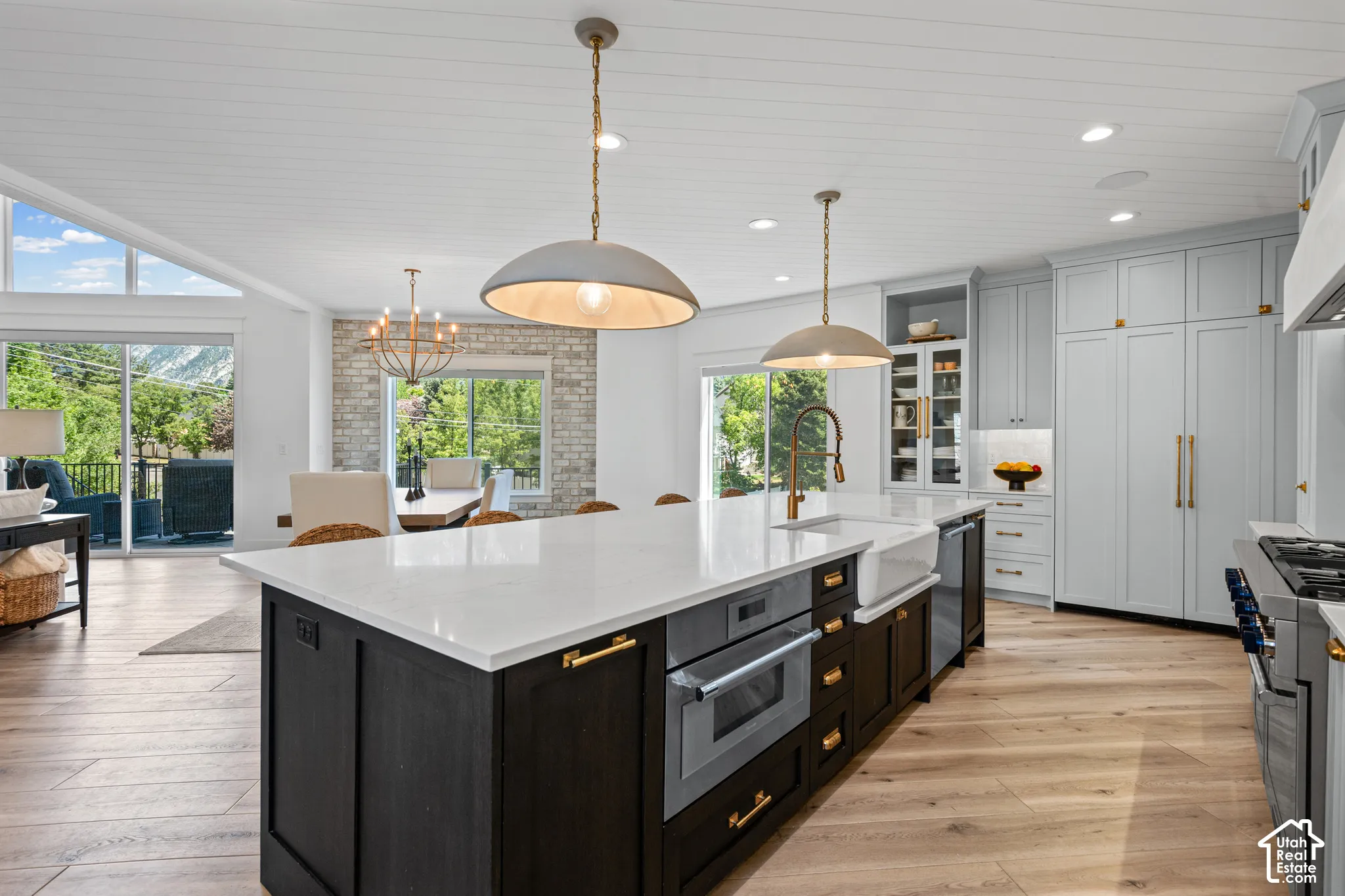 Spacious kitchen featuring a large central island with white countertop, integrated microwave, farmhouse-style sink, and gold-tone hardware