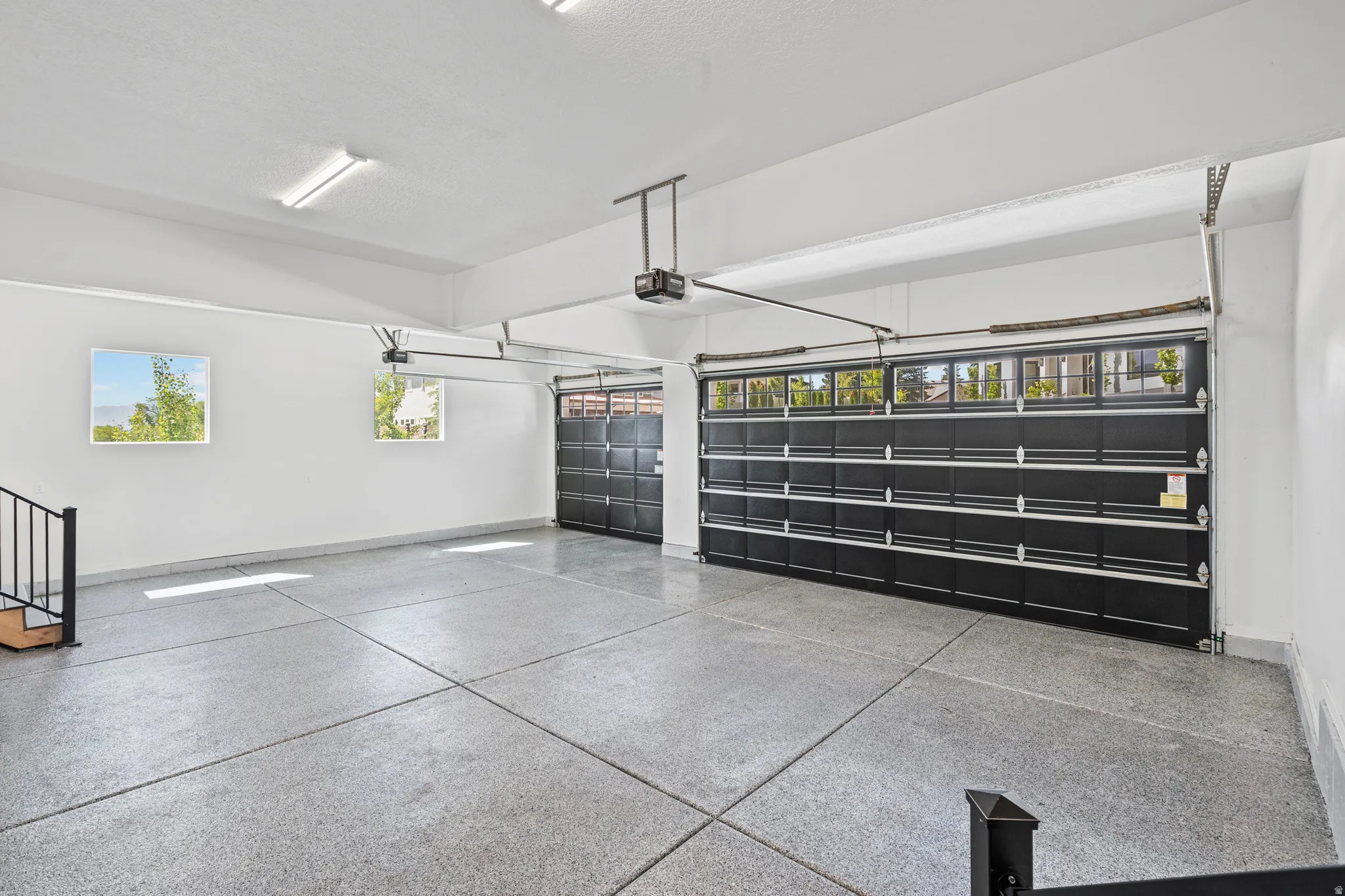 Spacious multi-car garage featuring epoxy-coated flooring, two overhead garage doors with frosted window panels, and multiple windows providing natural illumination