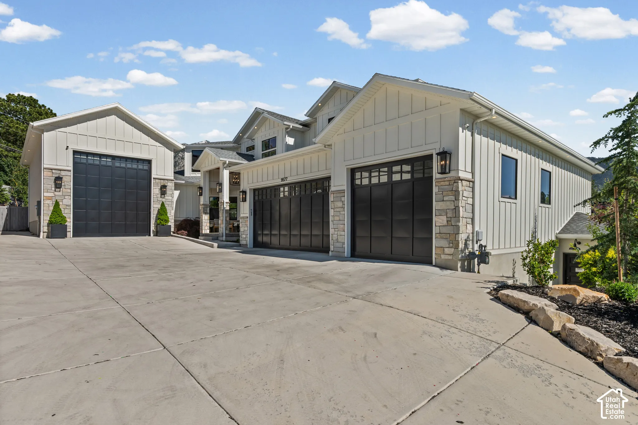 Modern farmhouse exterior featuring board and batten siding, stone accents, black-framed windows, multiple garage bays with dark paneled doors, and concrete driveway