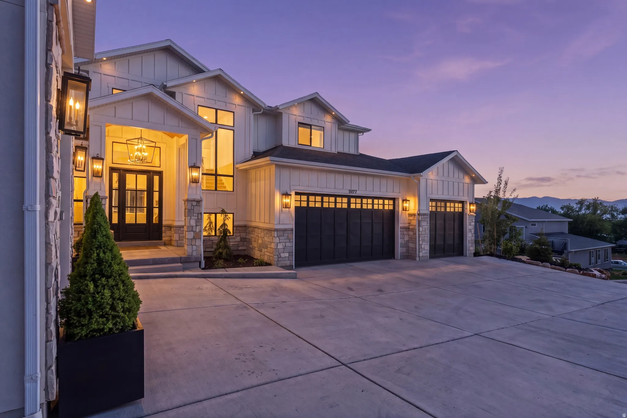 Modern farmhouse-style exterior featuring board and batten siding, stone accents, a prominent entry porch with a glass-paneled double door, and a three-car garage with dark paneled doors