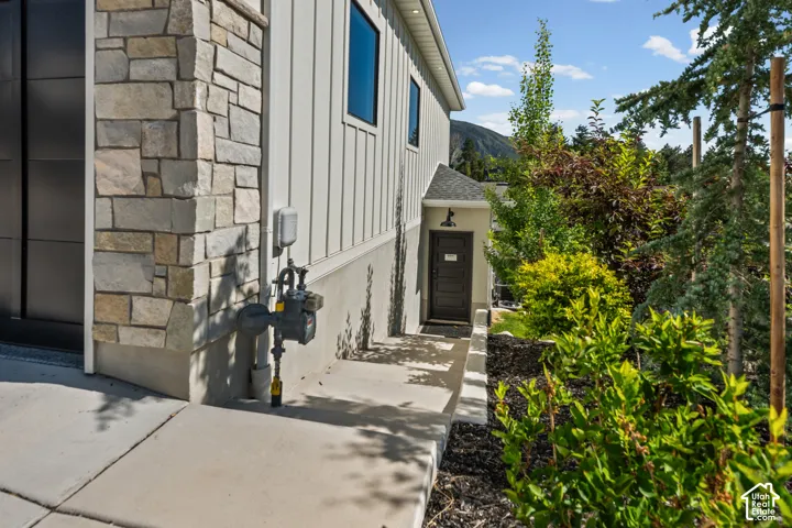 Exterior featuring a stone facade, vertical white siding, black-framed windows, a dark entry door, and established perimeter landscaping