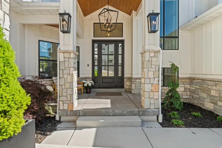 Entryway featuring a double door with glass panels, stone-clad pillars, board and batten siding, a wood-paneled ceiling, and large black-framed windows
