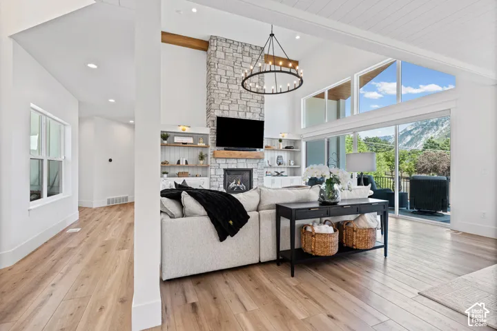 Spacious living area featuring a vaulted ceiling with exposed wood beam, stone fireplace with hearth, built-in shelving, and wood-finish flooring