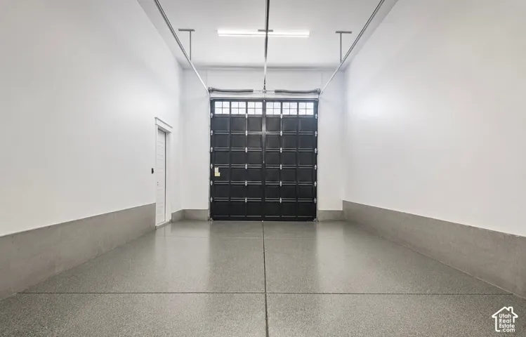 Spacious interior featuring a large black paneled door with window accents, light gray epoxy flooring, white walls, and a white side door