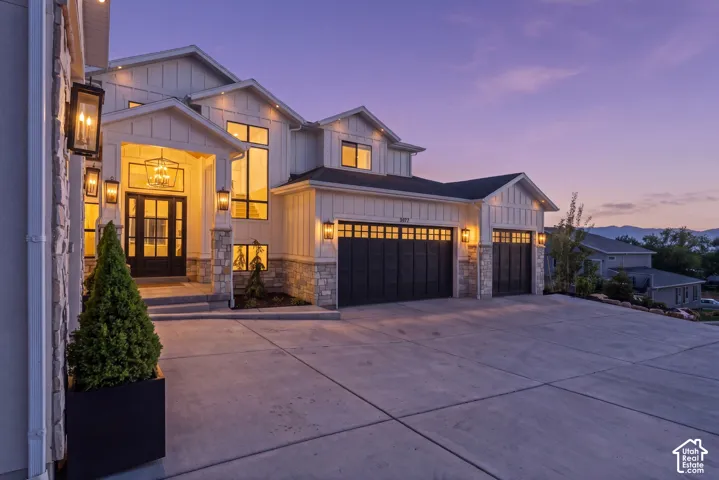 Modern farmhouse-style exterior featuring board and batten siding, stone accents, a prominent entry porch with a glass-paneled double door, and a three-car garage with dark paneled doors
