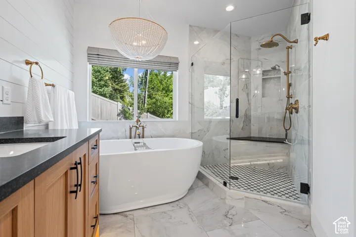 Freestanding soaking tub with brushed brass fixtures, glass-enclosed shower with black and white mosaic tile, and a wood-finish vanity with a dark countertop