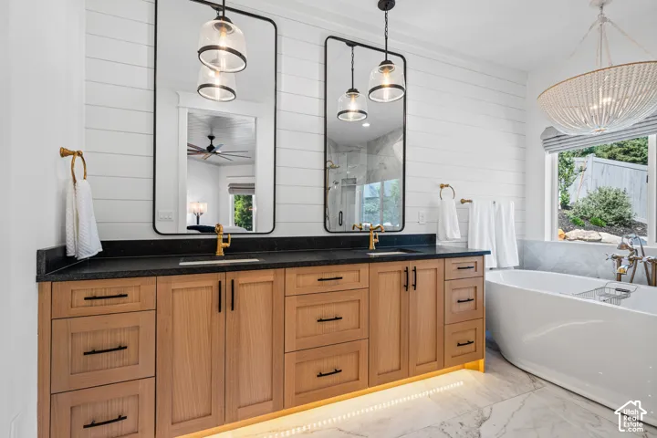 Bathroom featuring a dual vanity with wood-finish cabinetry, black countertops, and gold-tone fixtures