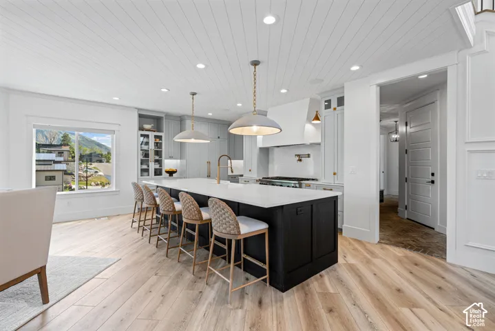 Spacious kitchen featuring a large island with seating, light wood-finish flooring, white shiplap ceiling, and light gray cabinetry