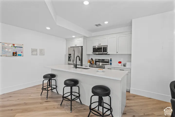 Bright kitchen featuring an expansive center island with seating, white shaker cabinetry, stainless steel appliances, and a tile backsplash