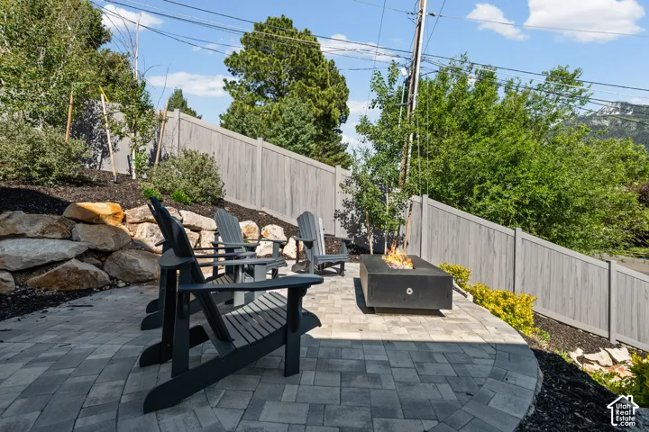 Paver patio featuring a built-in fire pit, privacy fencing, and a terraced landscape with natural rock retaining walls and mature plantings
