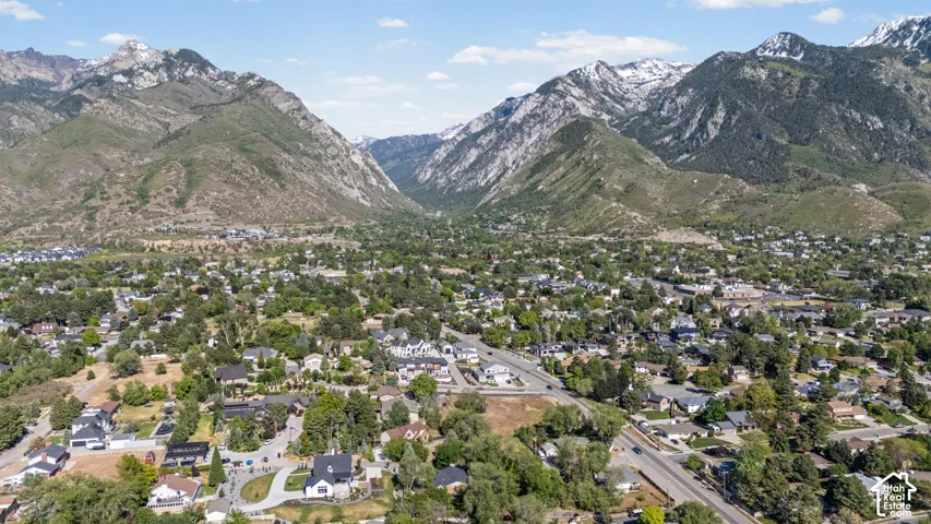 Expansive aerial perspective showcasing a residential community nestled at the base of majestic mountains, featuring a mix of mature trees and established homes
