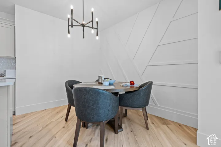 Dining area featuring a contemporary chandelier, accent wall with geometric millwork, wood-finish flooring, and white baseboards