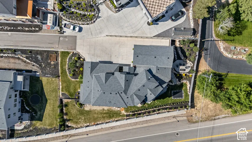 Contemporary residence featuring a multi-gabled gray shingle roof, extensive concrete driveway, landscaped grounds with established plantings, and a stone retaining wall