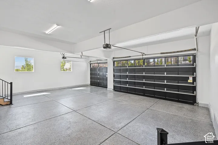 Spacious multi-car garage featuring epoxy-coated flooring, two overhead garage doors with frosted window panels, and multiple windows providing natural illumination
