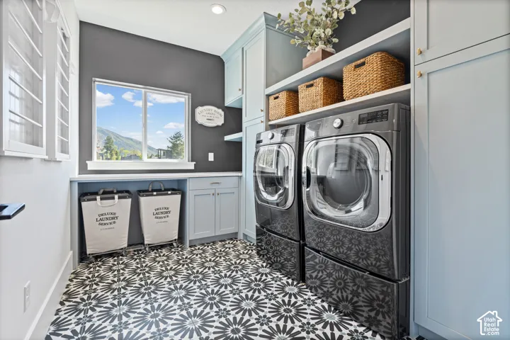 Laundry space featuring patterned tile flooring, light blue cabinetry, built-in shelving, and a dual window