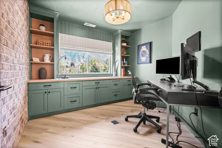 Dedicated office space featuring extensive built-in cabinetry with a natural wood countertop, open shelving, and light wood-finish flooring