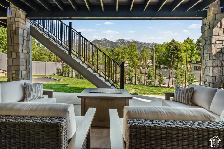 Covered patio featuring stone pillars, a concrete floor, an outdoor fire pit, and a prominent staircase with black metal railings leading to the upper level